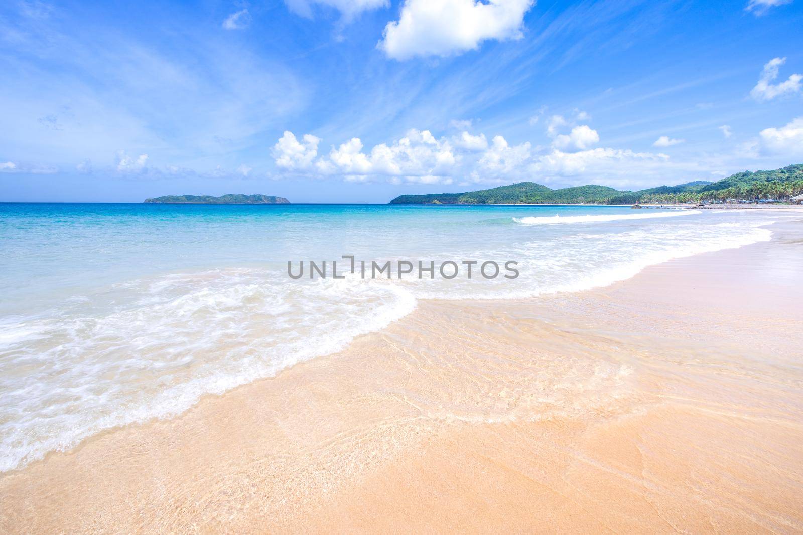 Beautiful amazing gold colored sandy beach with soft waves isolated with sunny blue sky. Concept of tropical calm tourism idea, copy space, close up