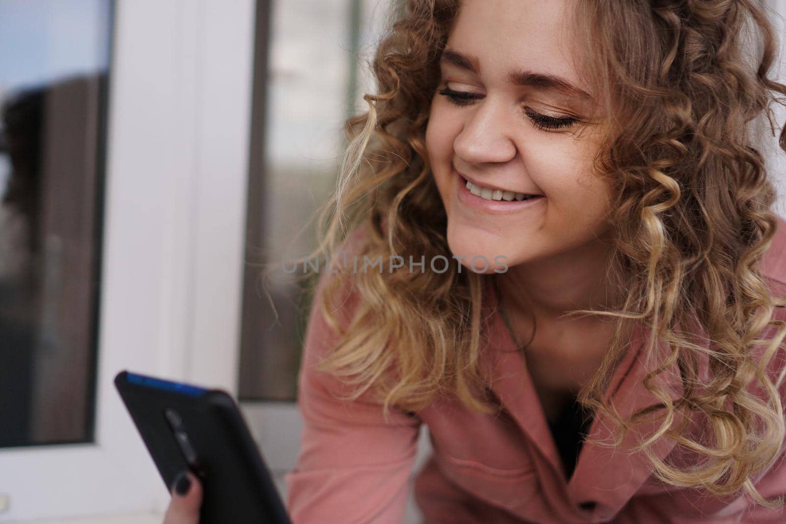 Cheerful gorgeous young woman with curly hair with smartphone by natali_brill