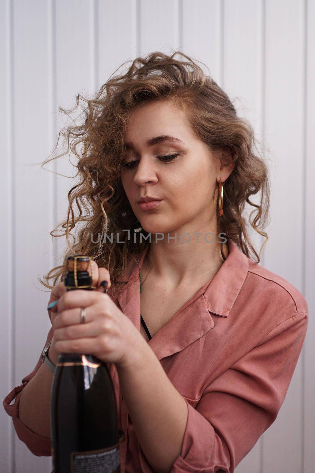 A young woman with curly hair opens a bottle of champagne by natali_brill