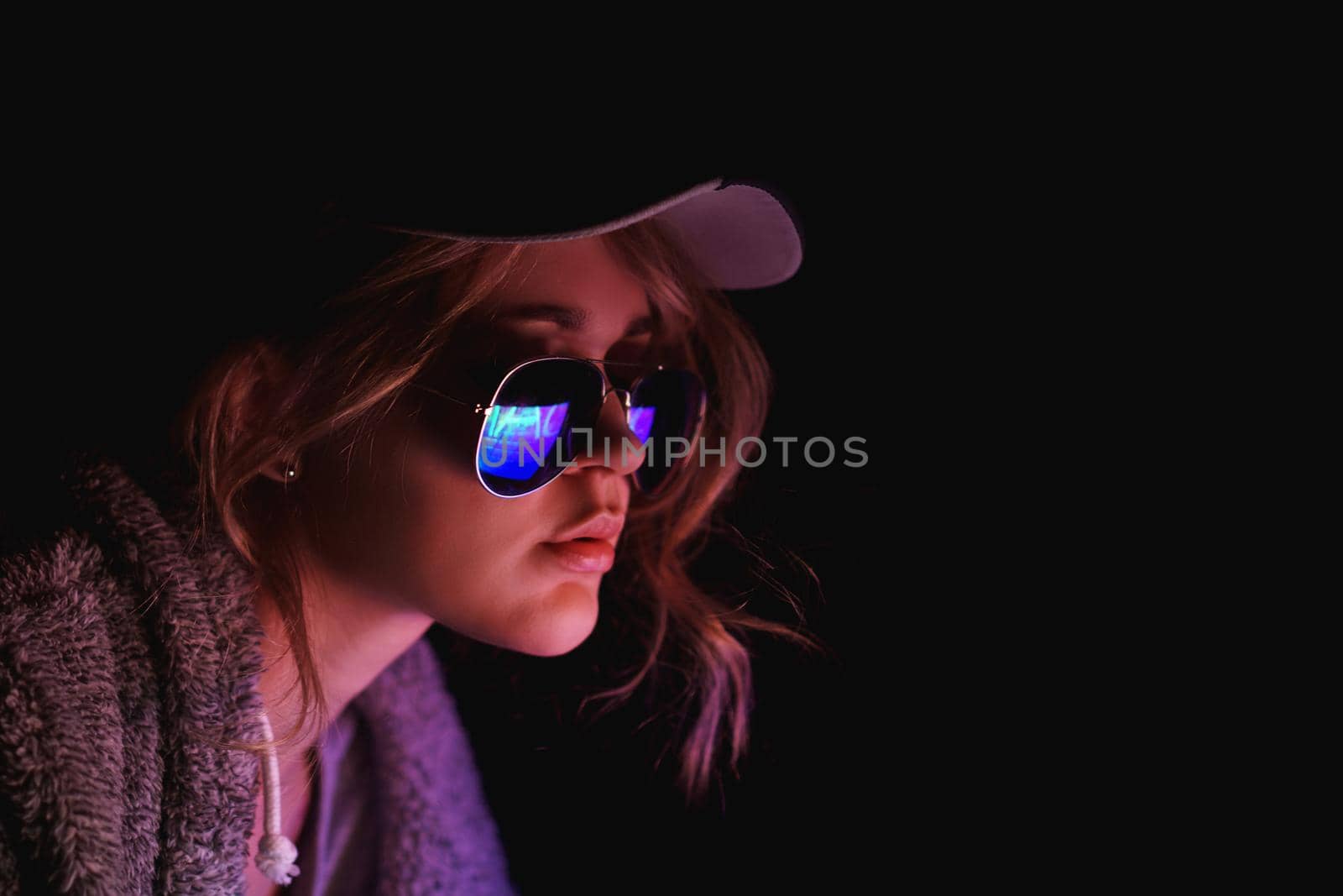 Hacker girl in a cap and sunglasses in front of a computer in neon light