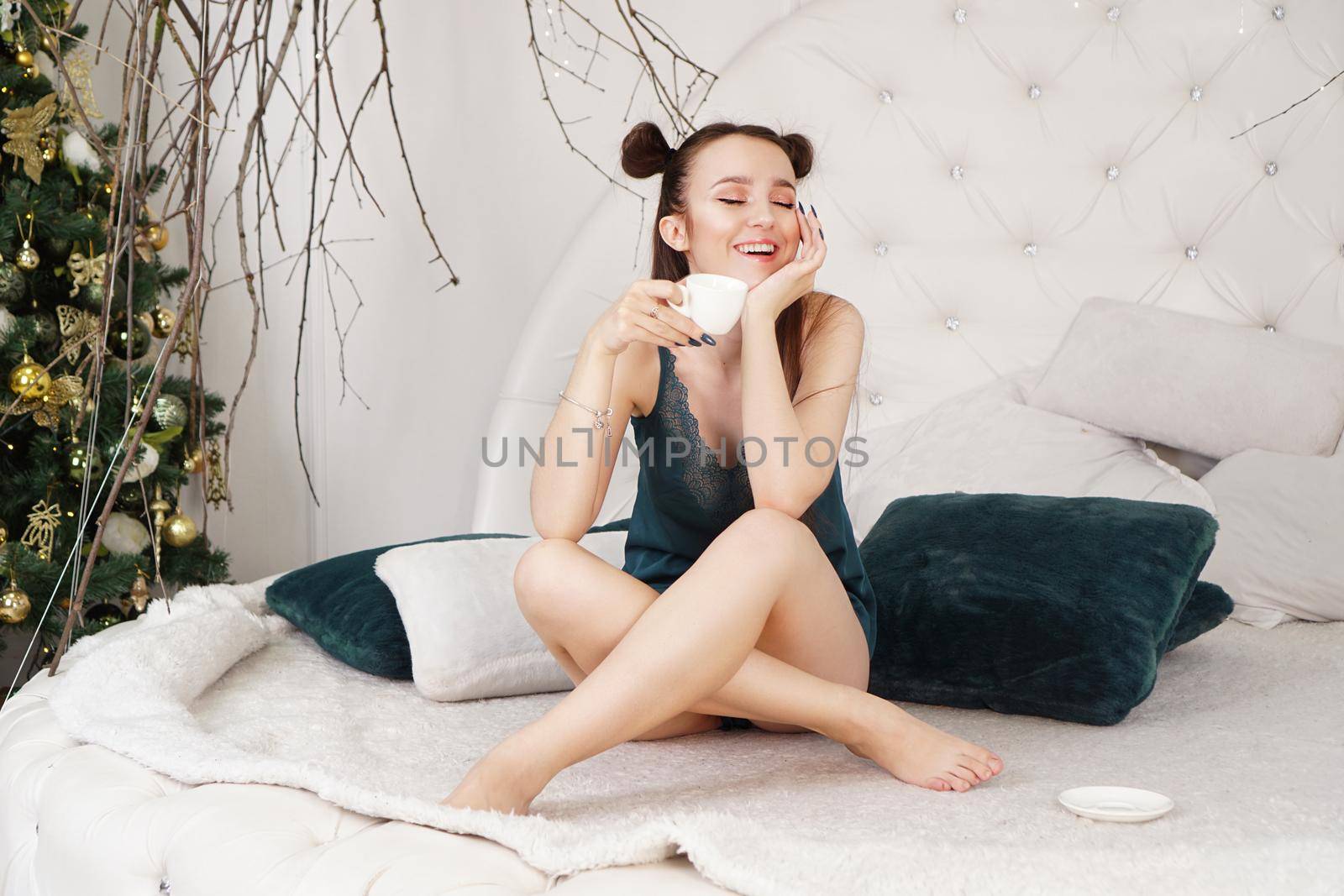 Happy young woman with cup of coffee or tea in bed at home bedroom - christmas morning time