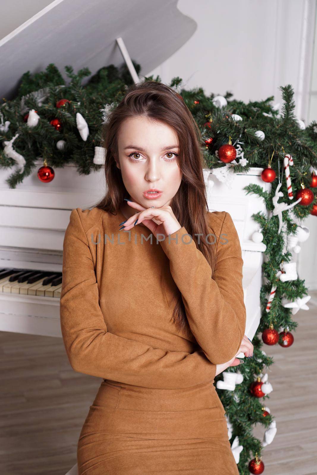 Beautiful girl with long blond hair near a white grand piano with christmas decor