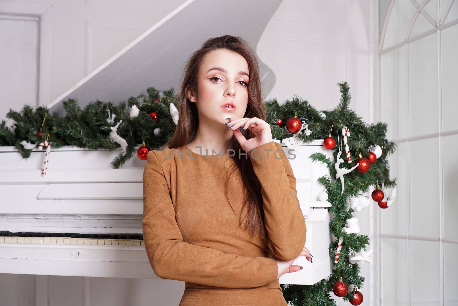 Beautiful girl with long hair near a white piano with Christmas decoration by natali_brill