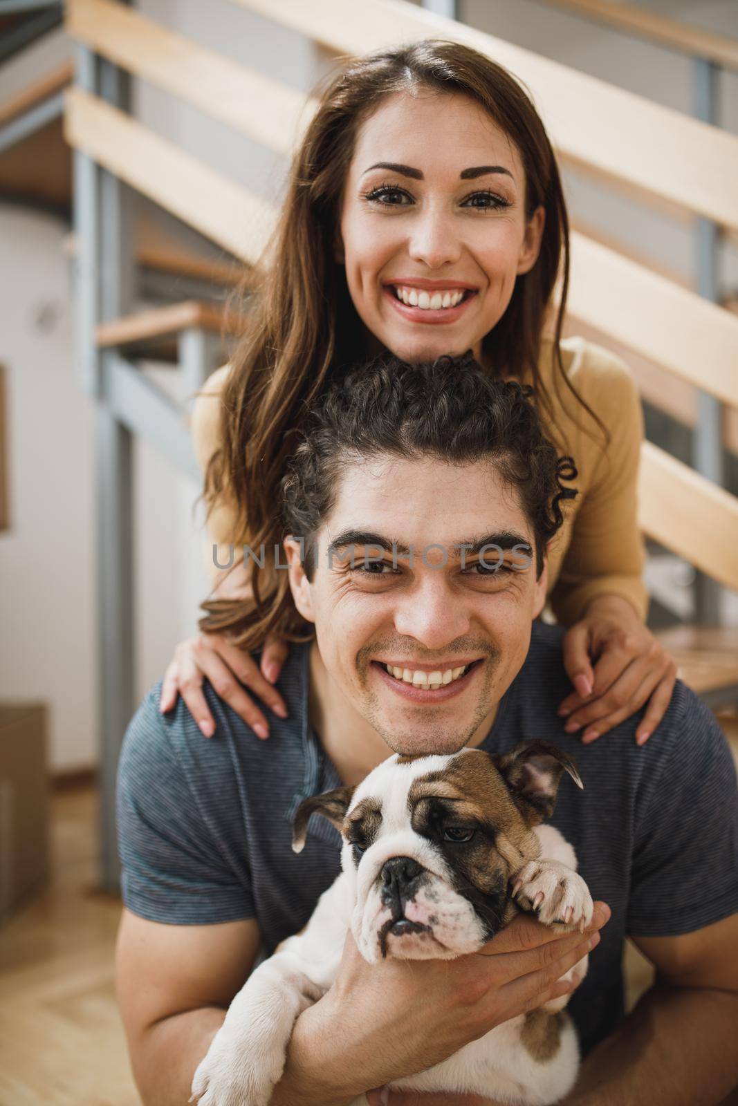 Portrait of a smiling young couple with their English bulldog puppy while moving into their new home. Looking at camera.