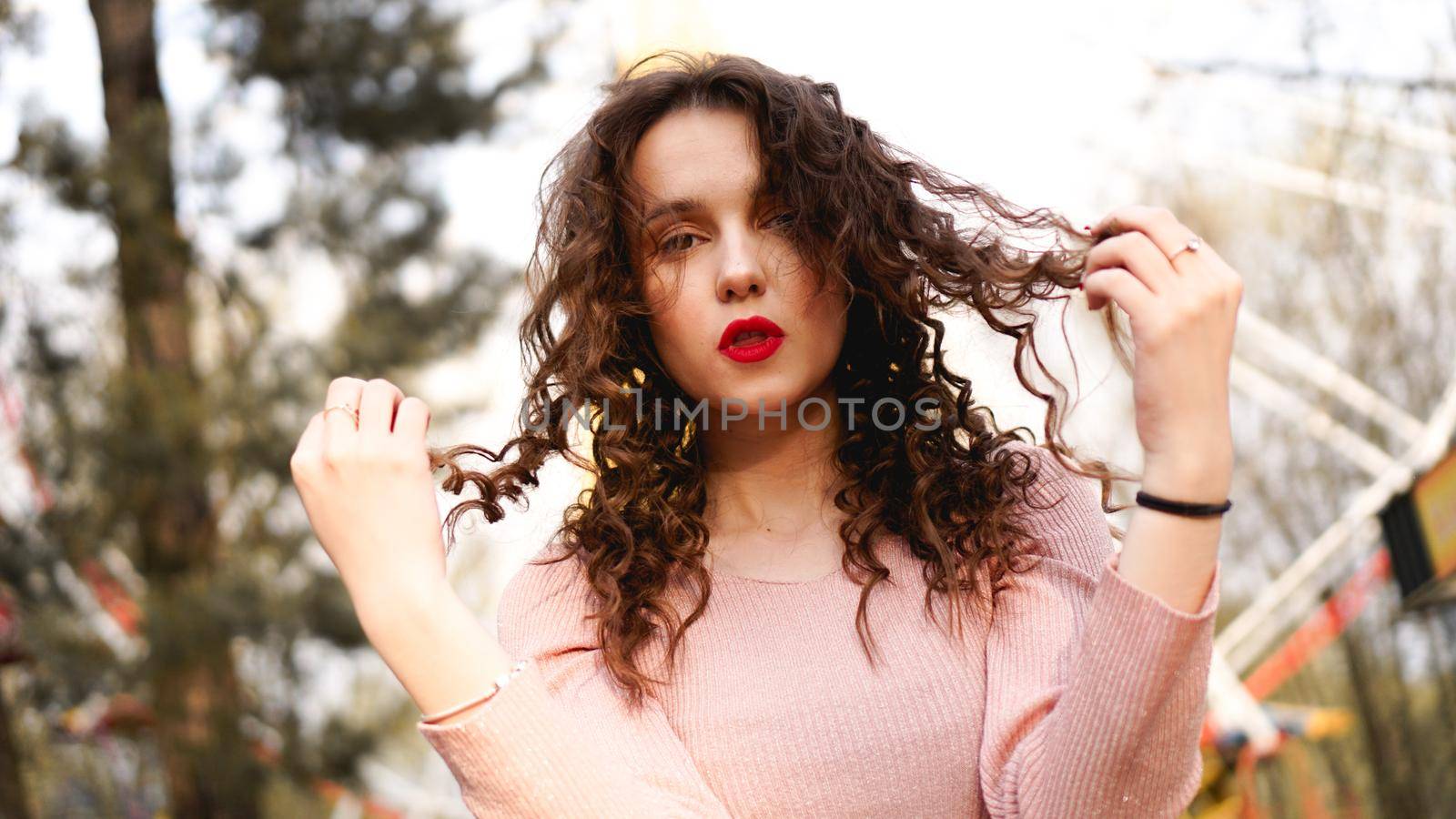 Women with long curly hair in the background of the Ferris wheel in sunny day