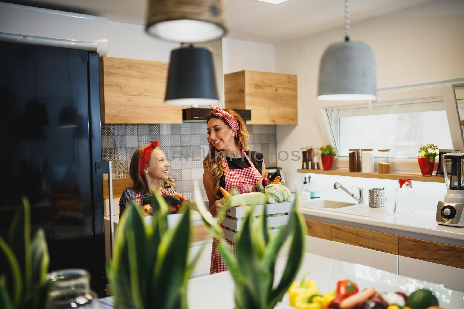A young cute girl helping her smiling mom preparing fresh vegetables in the theirs kitchen.