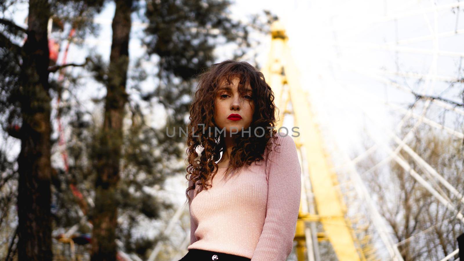 Women with long curly hair in the background of the Ferris wheel in sunny day
