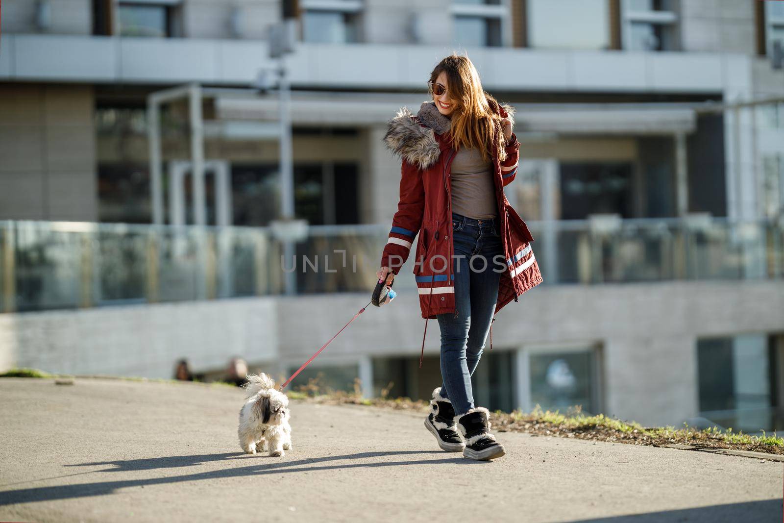 A smiling young woman walking with her cute Shih Tzu dog by the city street.
