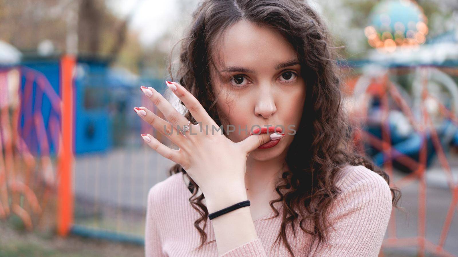 Stylish young hipster woman posing outdoors on the background of carousels. Girl enjoys a summer day