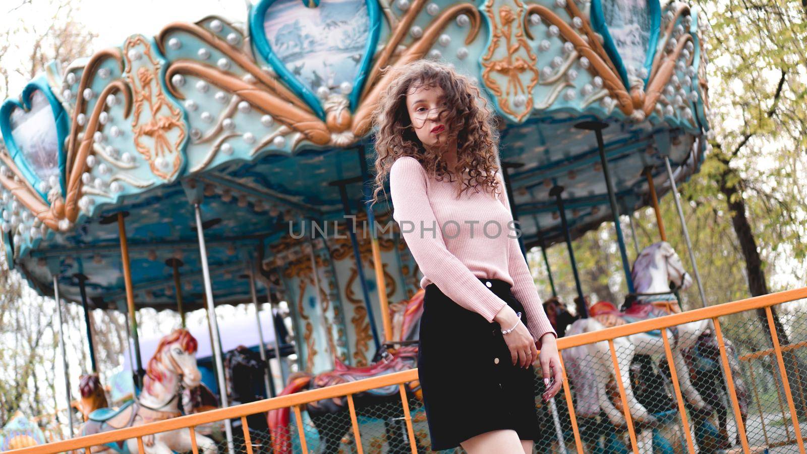 Stylish young hipster woman posing outdoors on the background of carousels. Girl enjoys a summer day