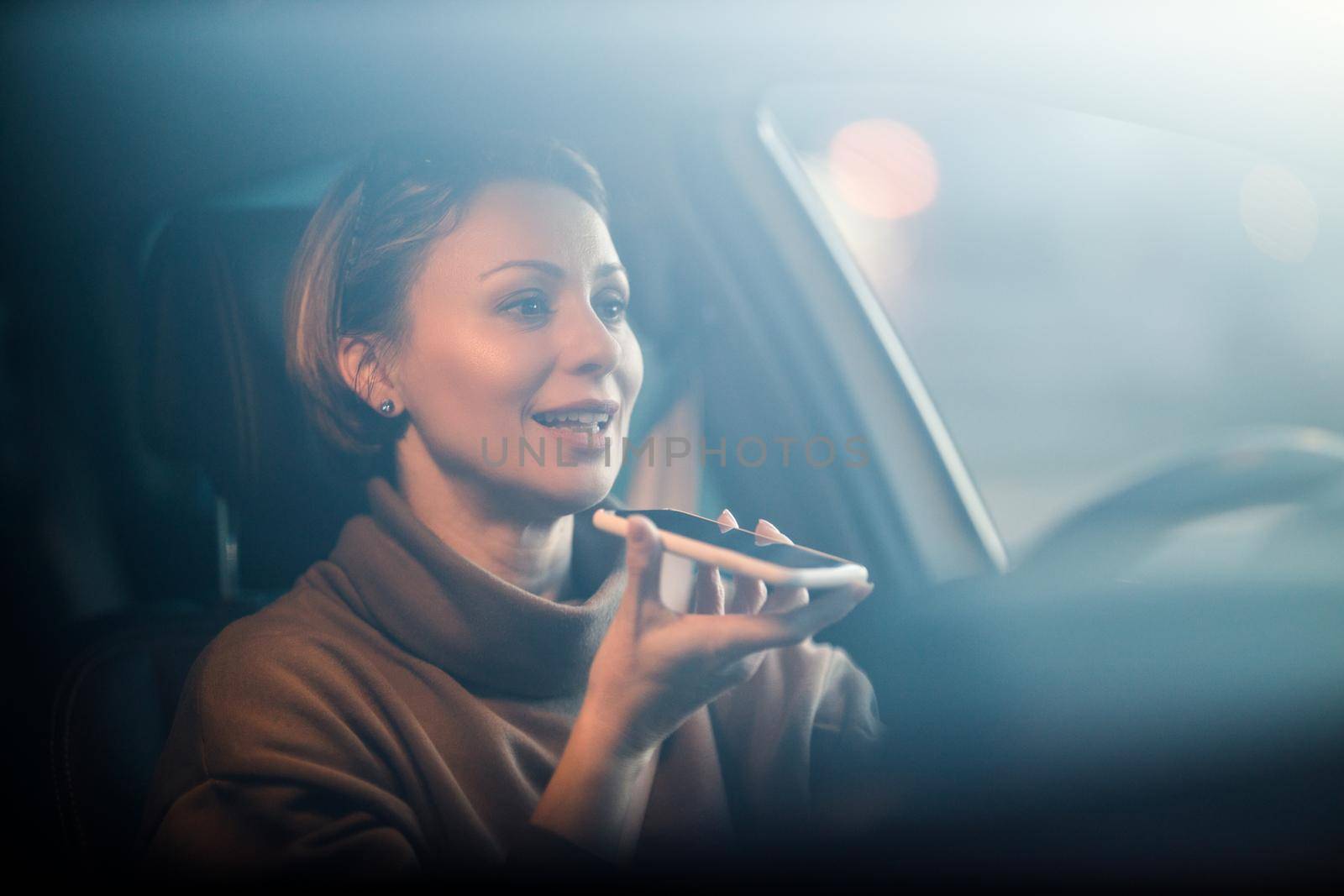 A beautiful mature woman talking voice message on a smart phone while driving her car.
