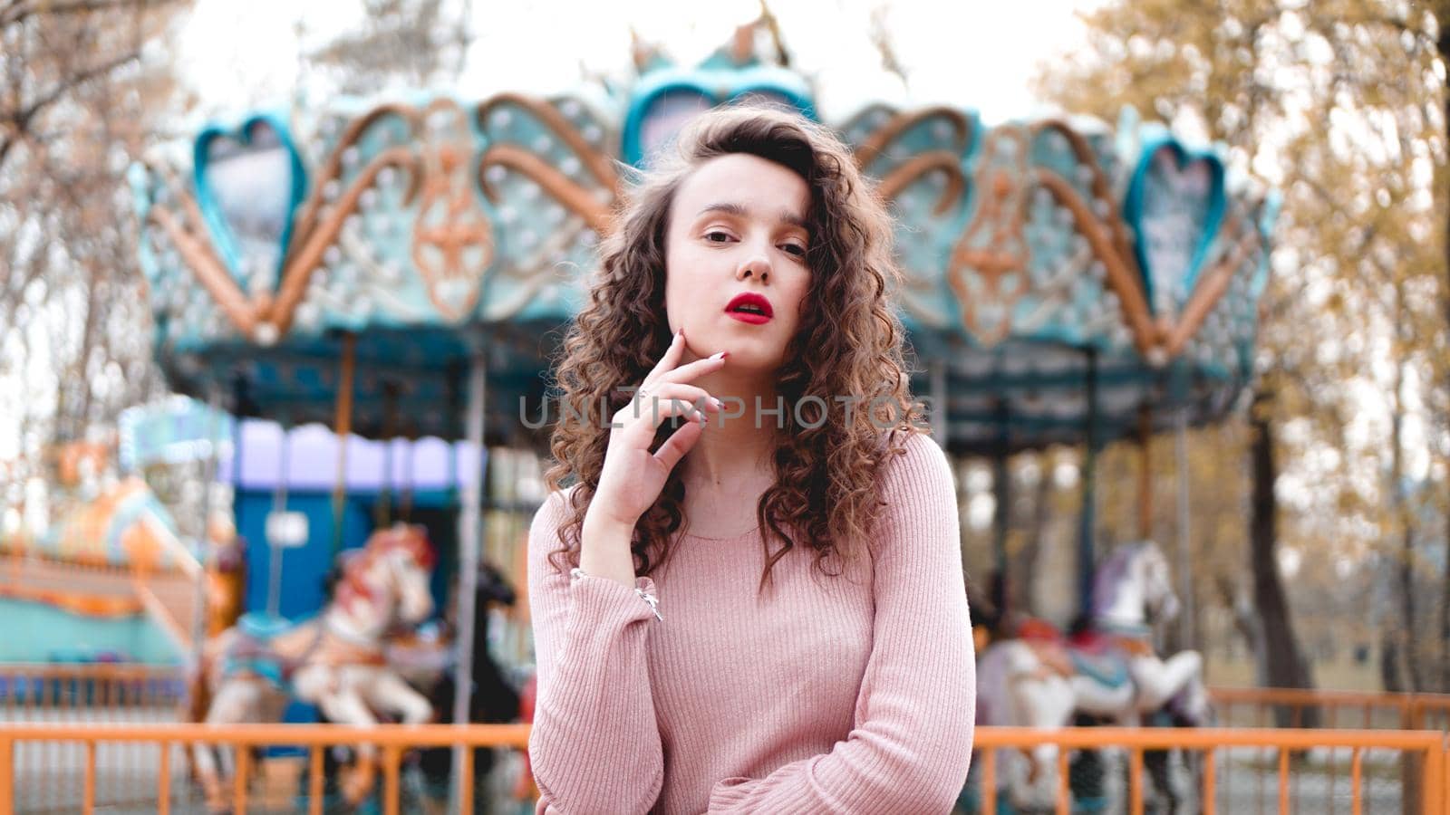 Stylish young hipster woman posing outdoors on the background of carousels. Girl enjoys a summer day