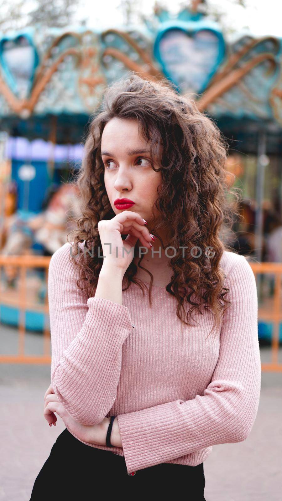 Stylish young hipster woman posing outdoors on the background of carousels. Girl enjoys a summer day