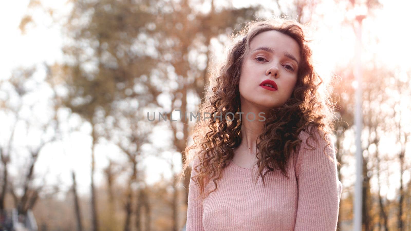 Closeup of a beautiful young woman with curly hair - a sunset behind her