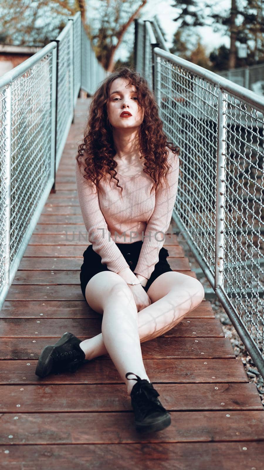 Fashion portrait of trendy young woman sitting near the netting rabitz in the city