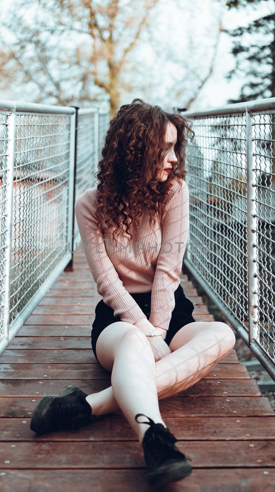 Fashion portrait of trendy young woman sitting near the netting rabitz in the city