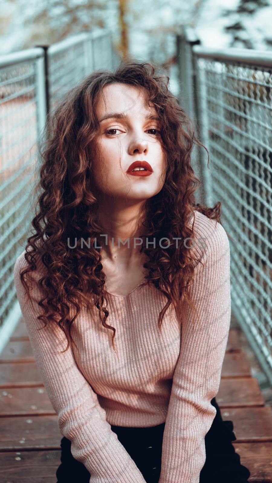 Fashion portrait of trendy young woman sitting near the netting rabitz in the city