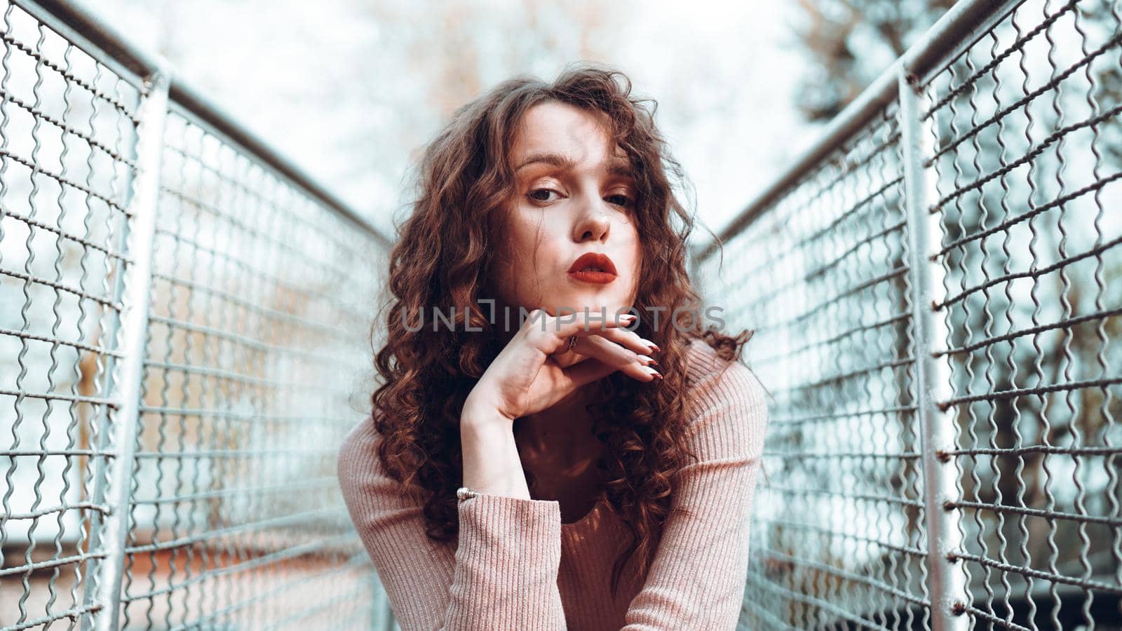 Fashion portrait of trendy young woman sitting near the netting rabitz in the city