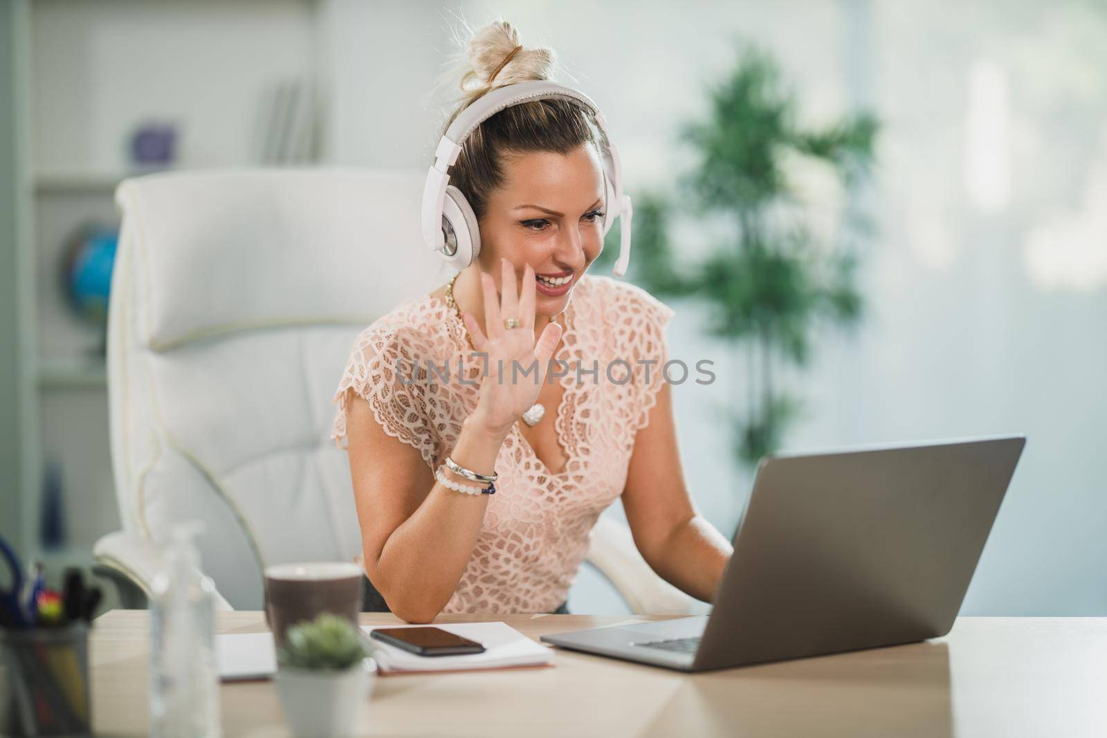 An attractive business woman working in a call center and waving to client over a video call at her laptop.