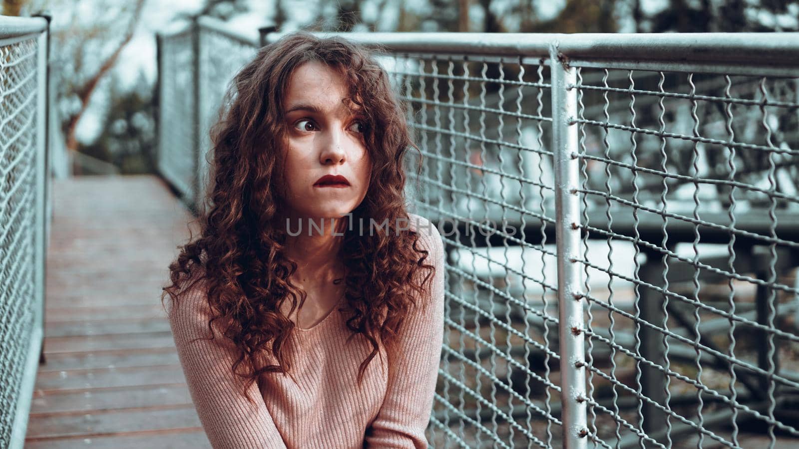 Fashion portrait of trendy young woman sitting near the netting rabitz in the city