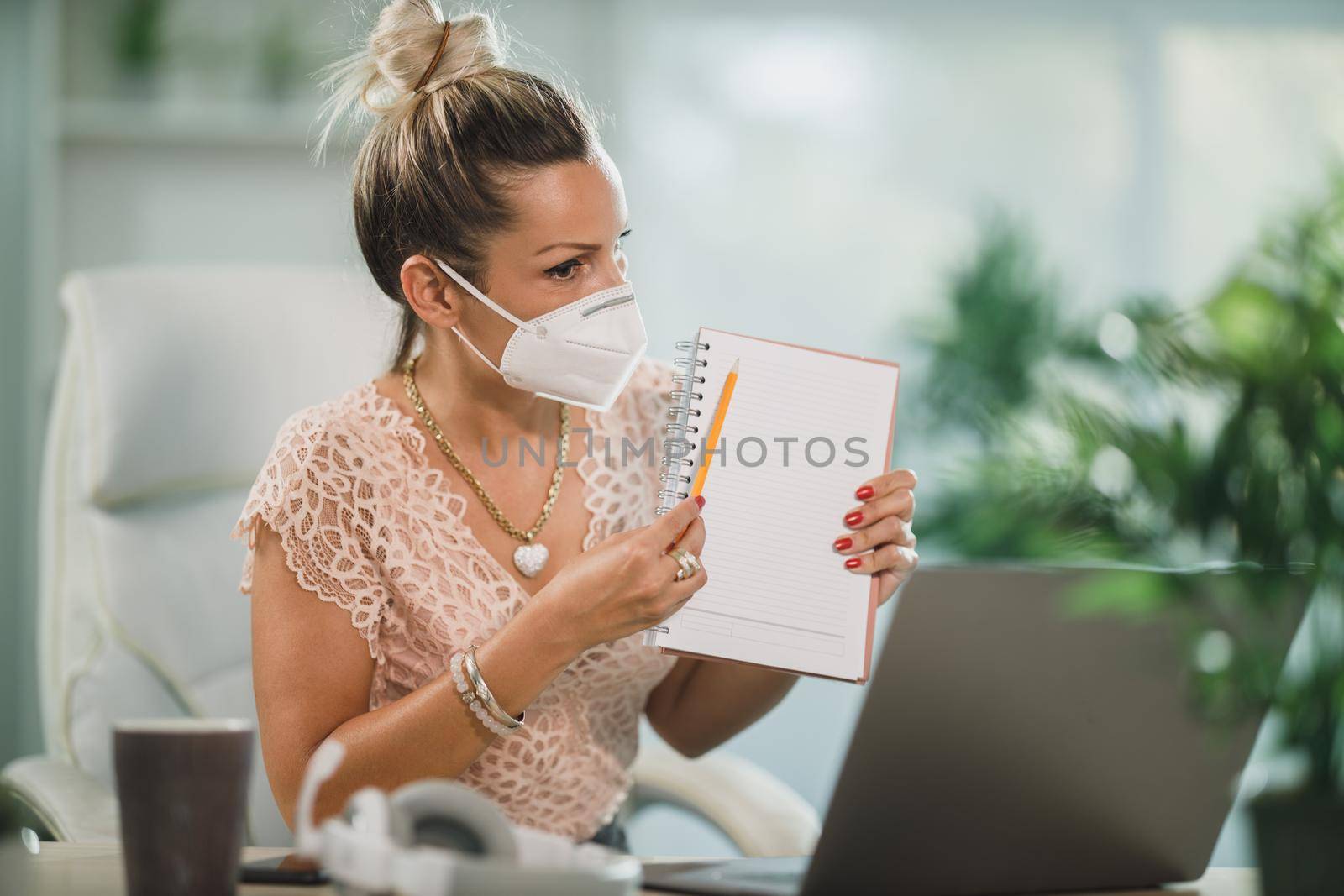 An attractive business woman with N95 protective mask working in a call center and talking with client online at her laptop.