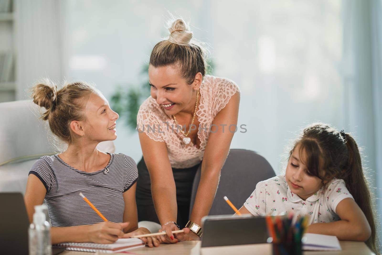 A beautiful single mother helping hers two daughters with homework at home.