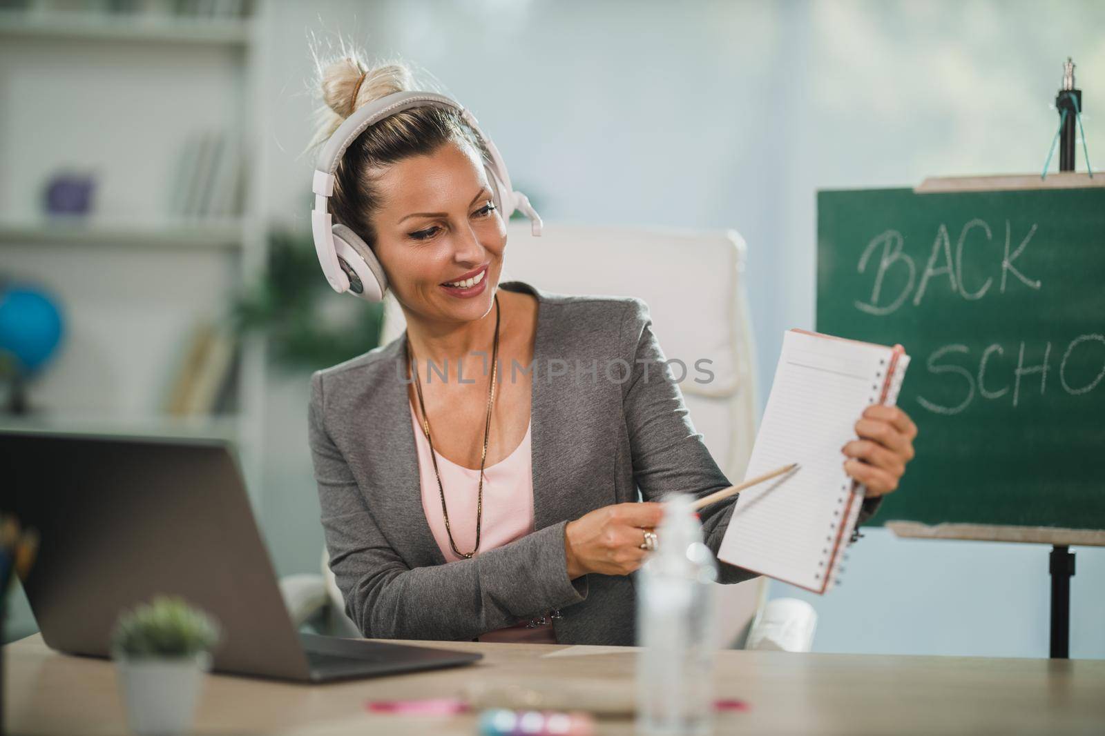 A smiling young woman making video call at her laptop and teaching students online in her home office.