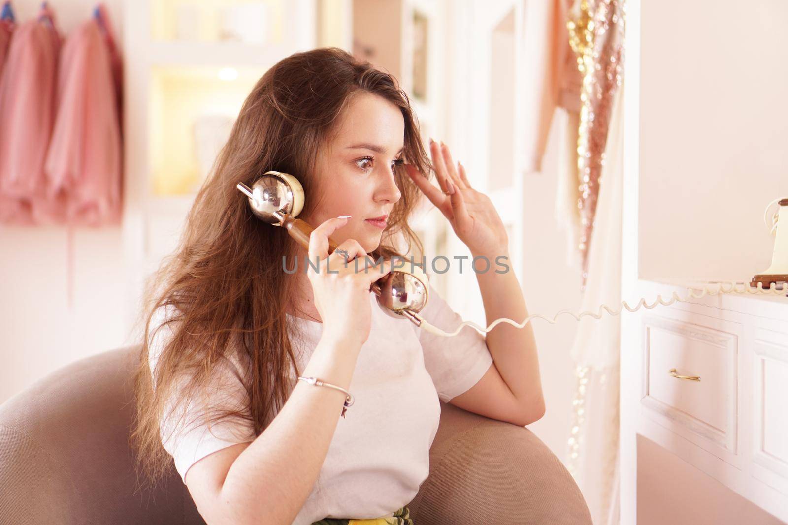 A surprised woman talks on the phone. phone handset in retro style. The girl in the dressing room in pink color