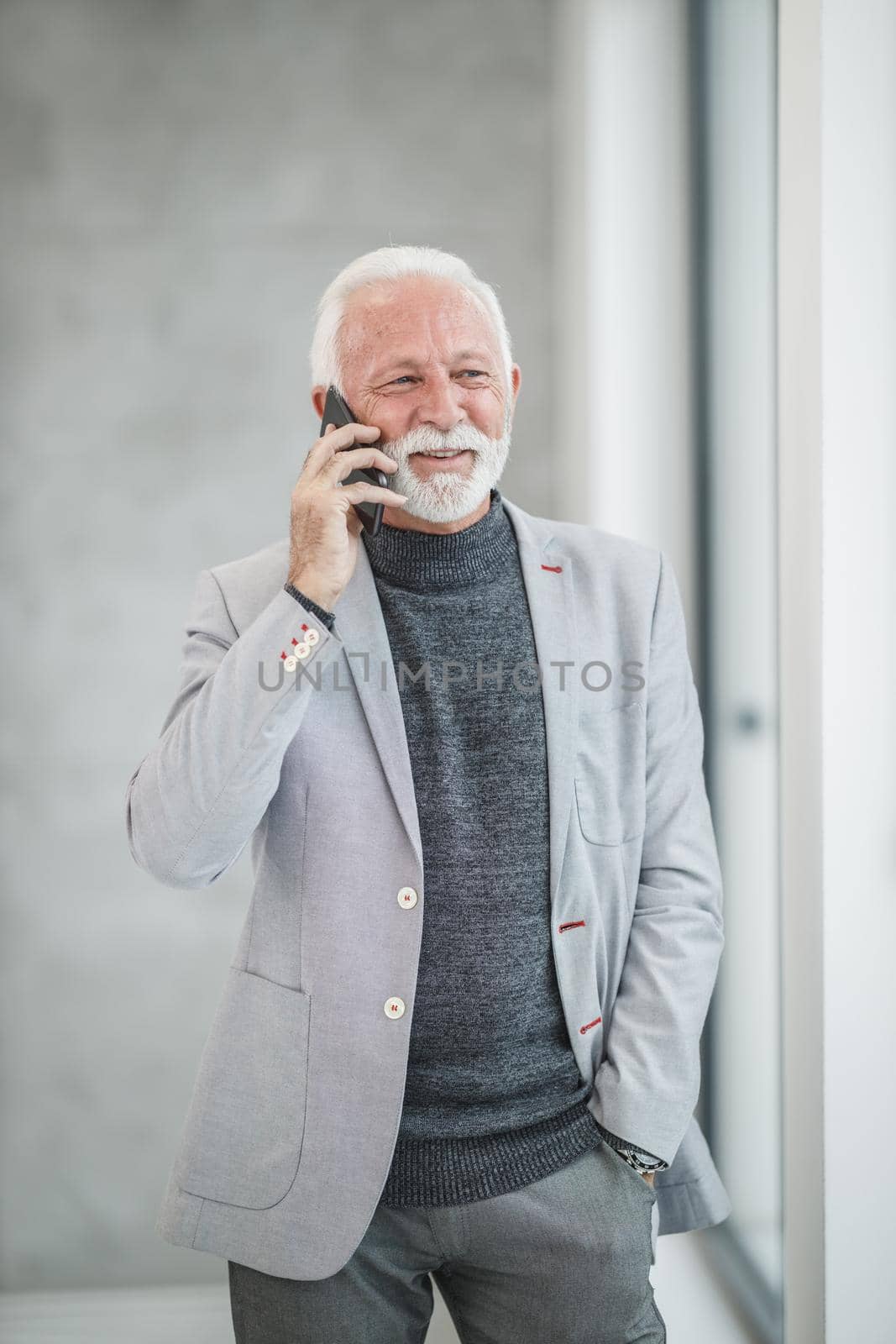 Portrait of a confident senior businessman talking on a smart phone while standing in a modern office.