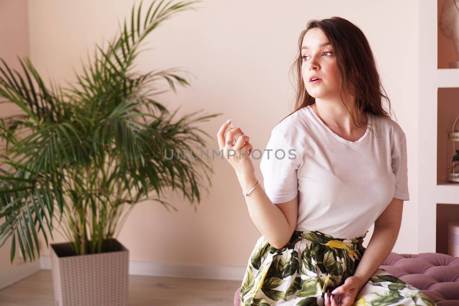 Beautiful young woman with bottle of perfume at home - pink dressing room