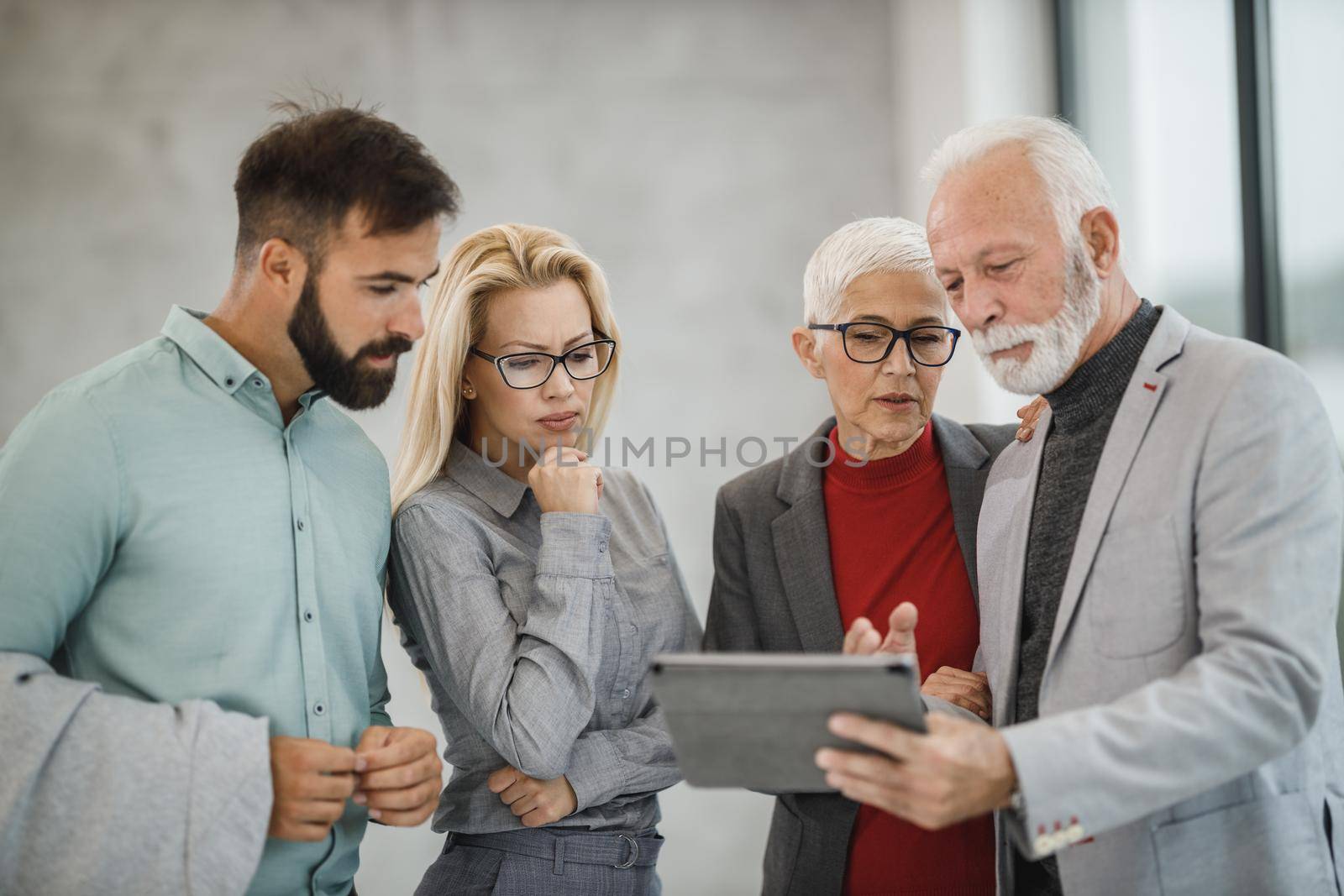 A group of confident business people using digital tablet  and having a discussion with each other during the meeting in a modern office.