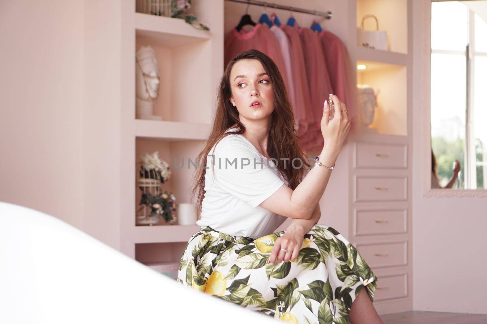 Beautiful young woman with bottle of perfume at home - pink dressing room