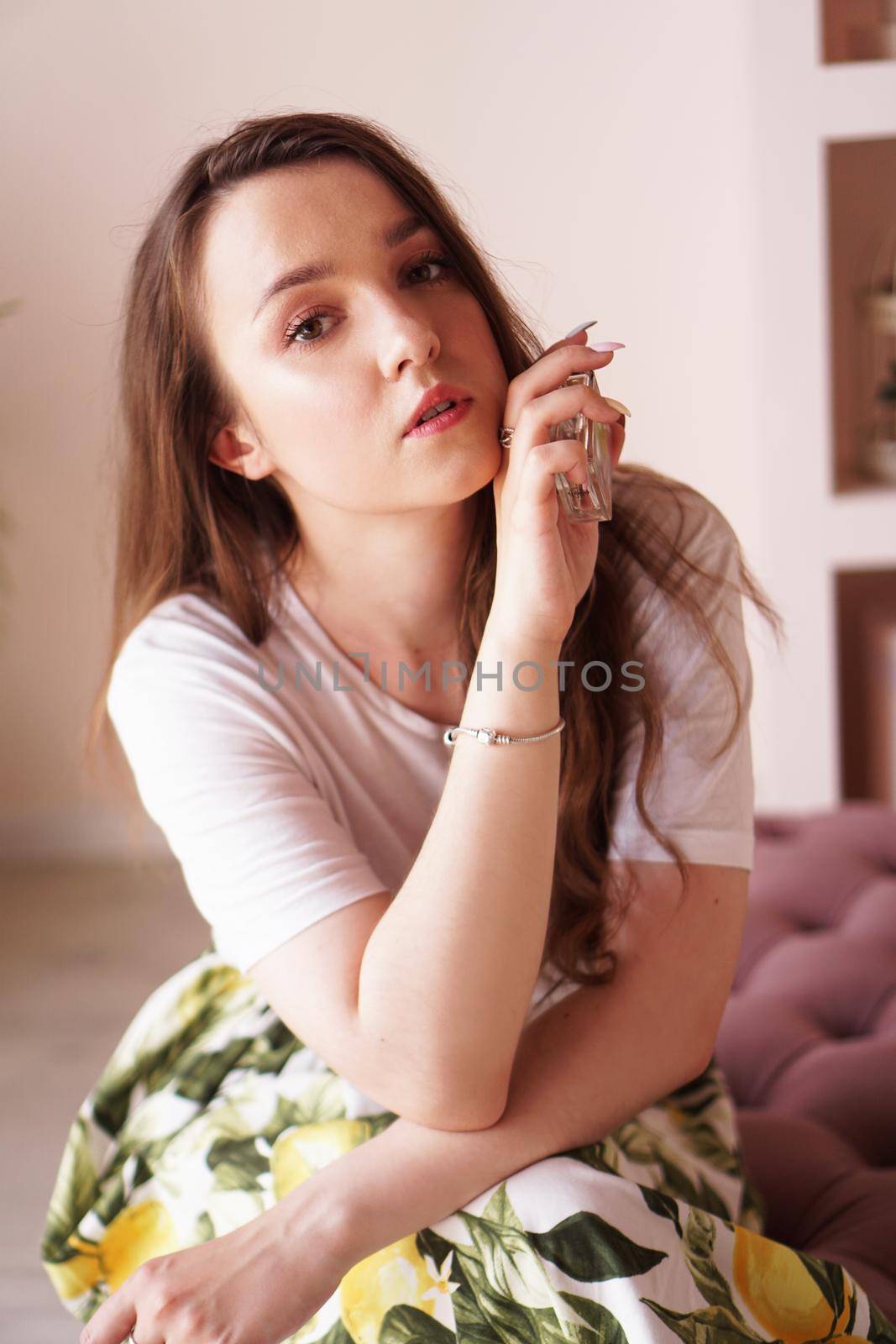 Beautiful young woman with bottle of perfume at home - pink dressing room