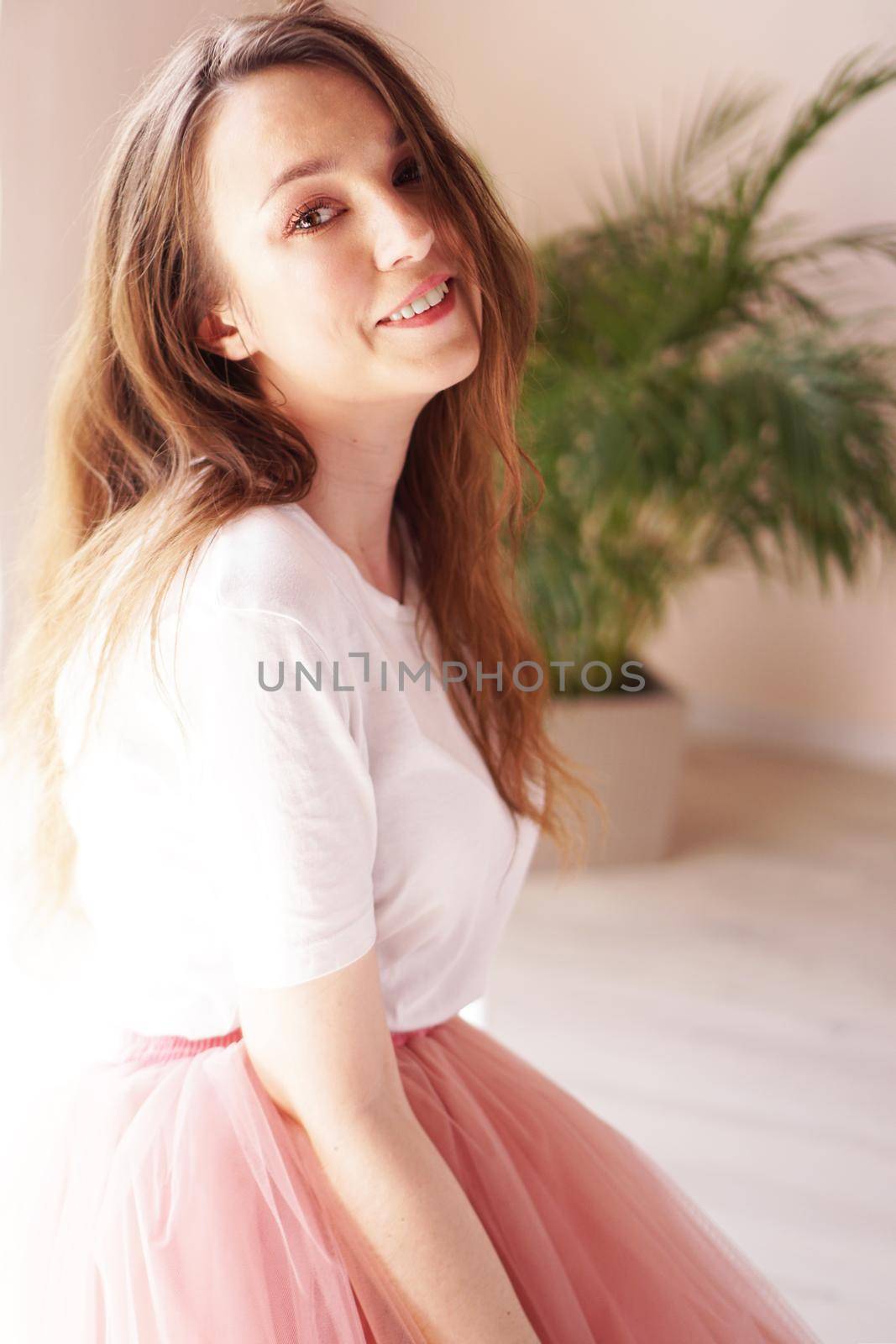 Fashion portrait. Attractive woman in pink skirt and white t-shirt looking at camera - soft colors of interior
