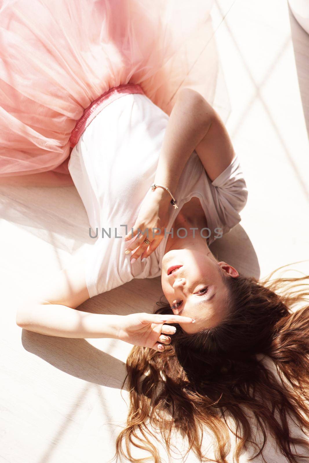 A portrait of a young woman in beautiful sunlight from window. She lies on a wooden floor.