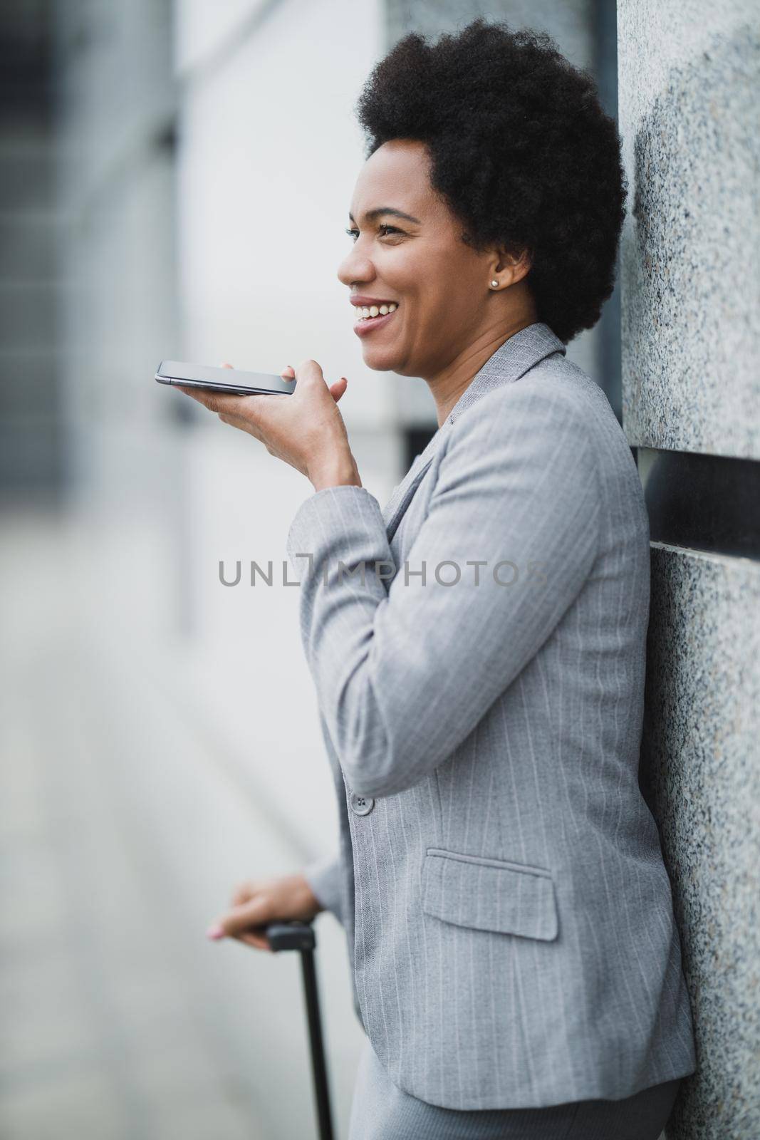 A successful black business woman talking voice message on a smart phone during quick break in front a corporate building.