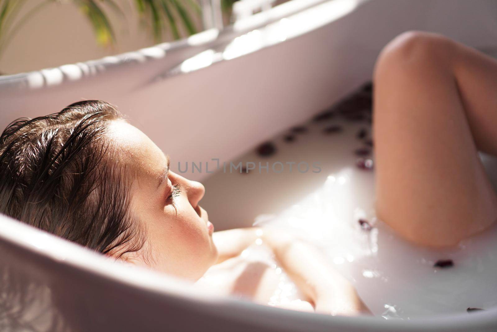 An Attractive girl relaxing in bath with petals on light background