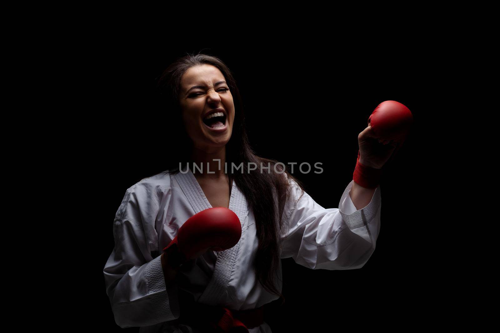 karate girl smiling in kimono and red gloves against black background