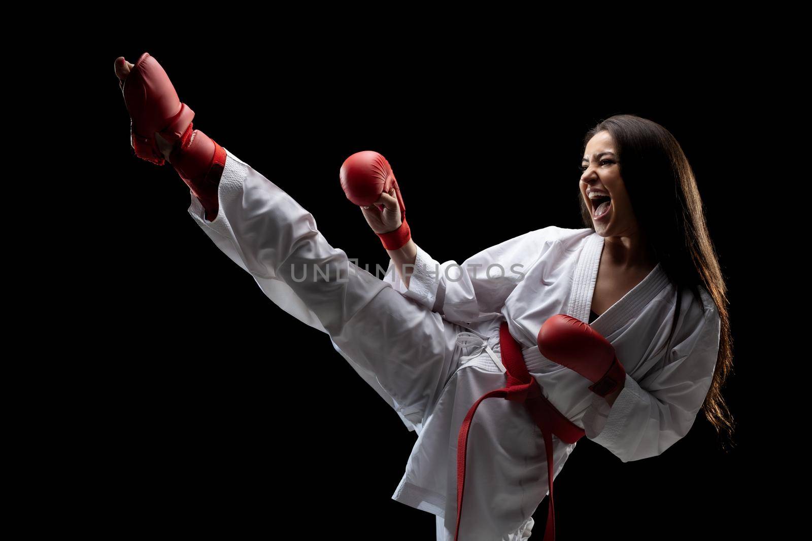 girl exercising karate leg kick and screaming against black background by kokimk