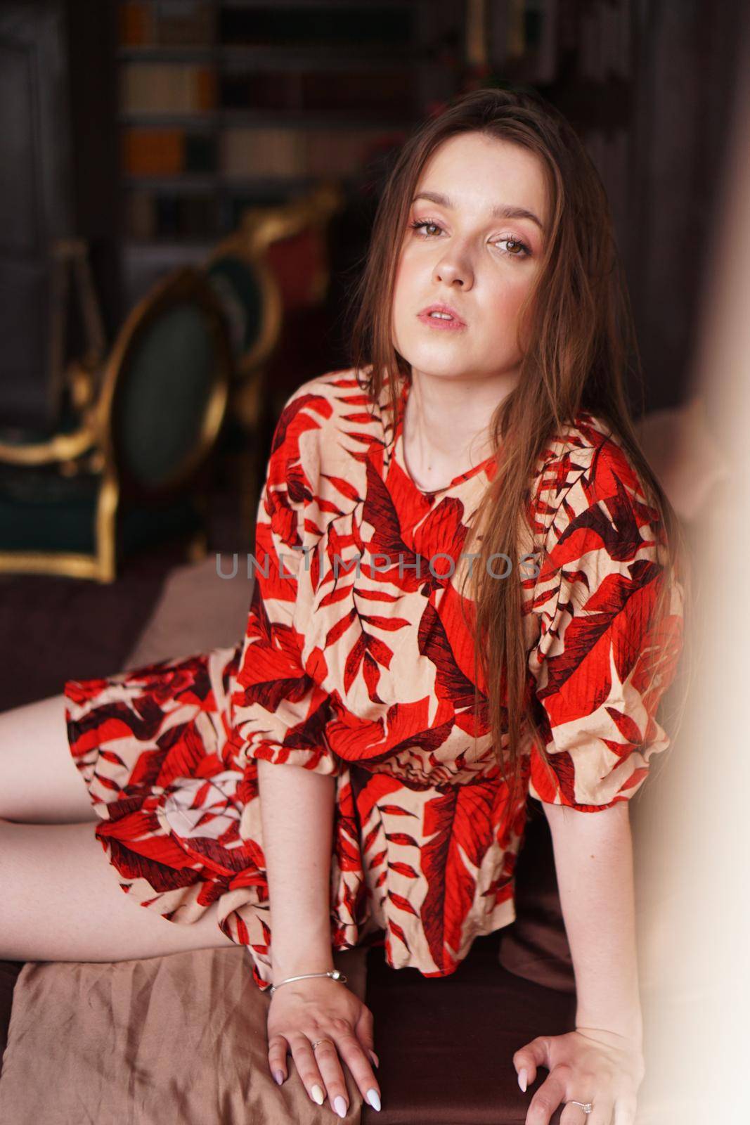 Relaxed woman lying on a brown bed thinking deeply. Woman in retro style room in red dress