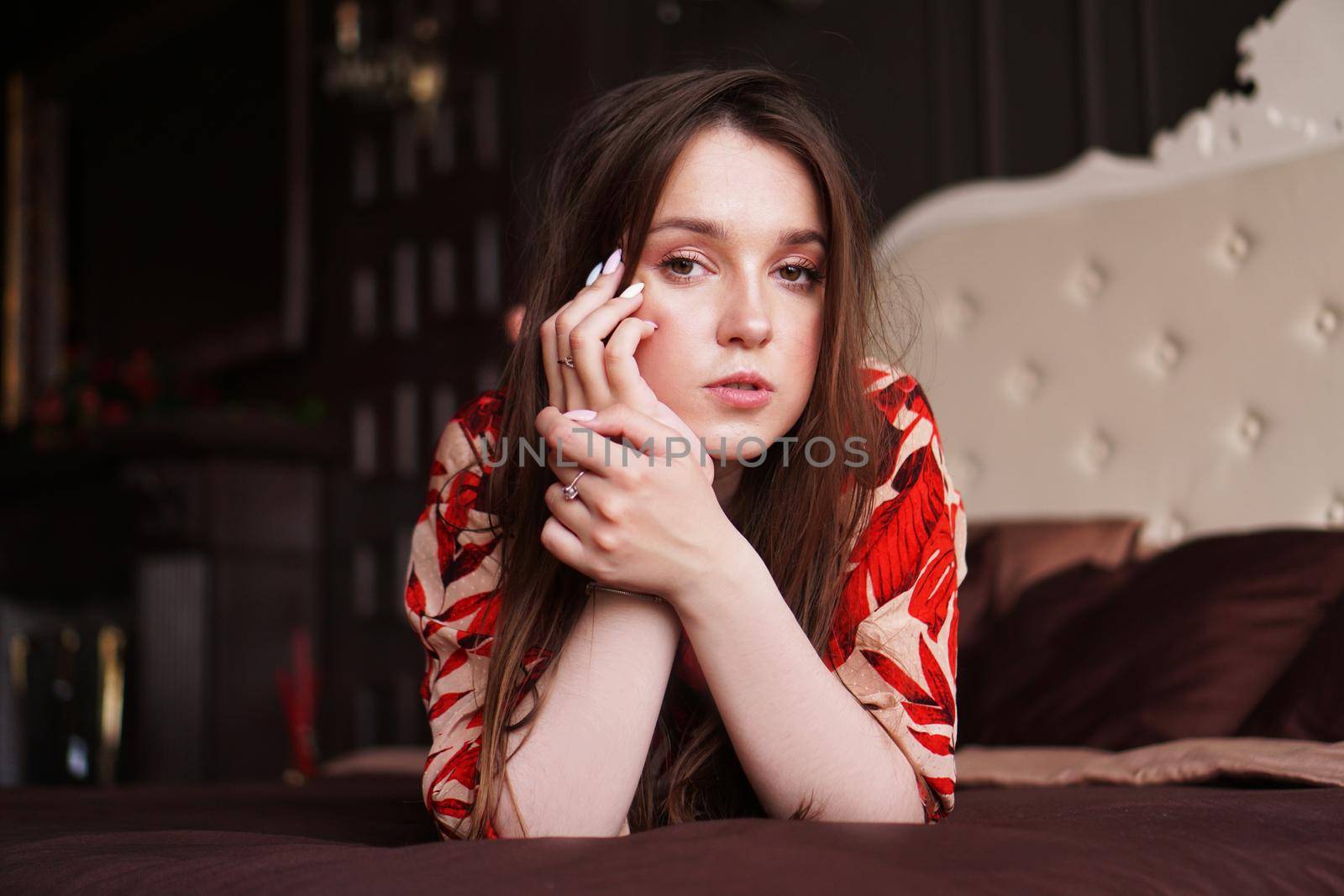 Relaxed woman lying on a brown bed thinking deeply. Woman in retro style room in red dress