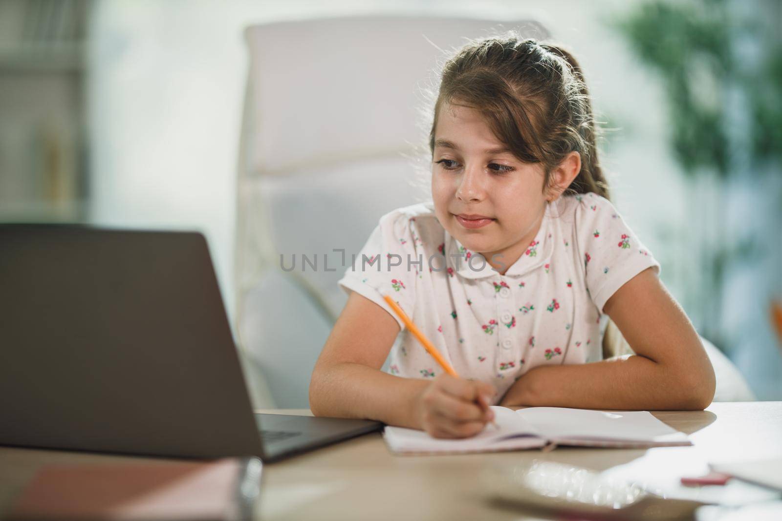 A cute little girl using her laptop to do a online lesson at home.
