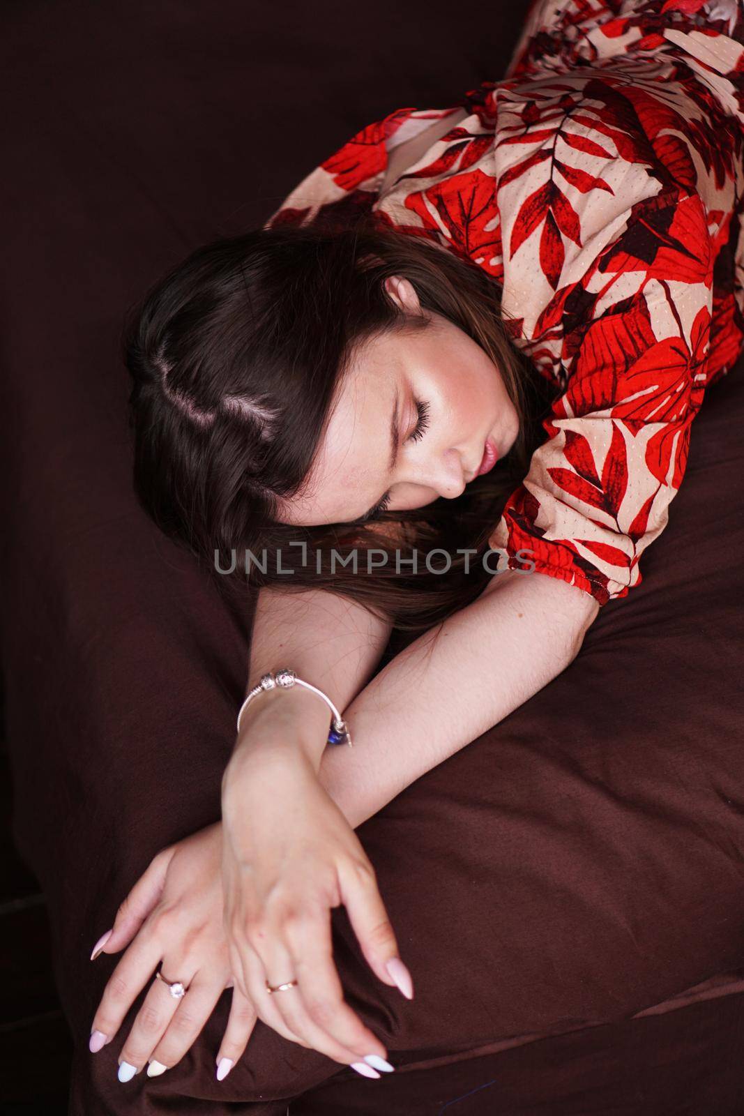 Relaxed woman lying on a brown bed. Woman in retro style room in red dress