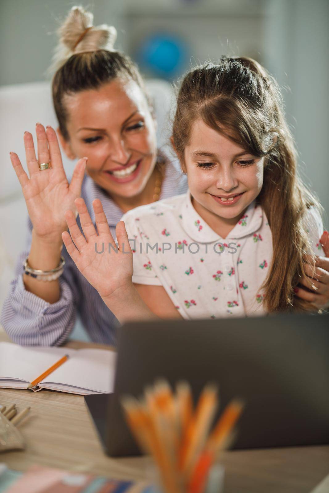 A cute little girl using and her beautiful single mother laptop and waving to their friends over a video call.