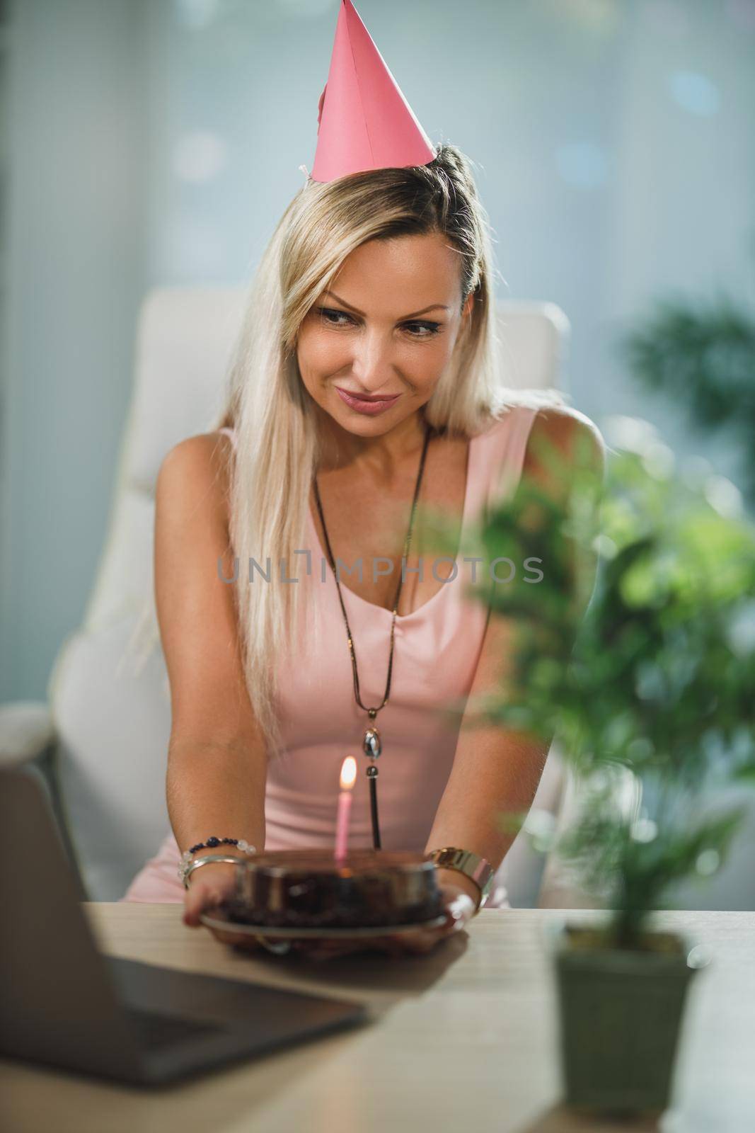 Alone attractive woman holding a birthday cake and have video call with friends while birthday celebration at home during pandemic isolation.