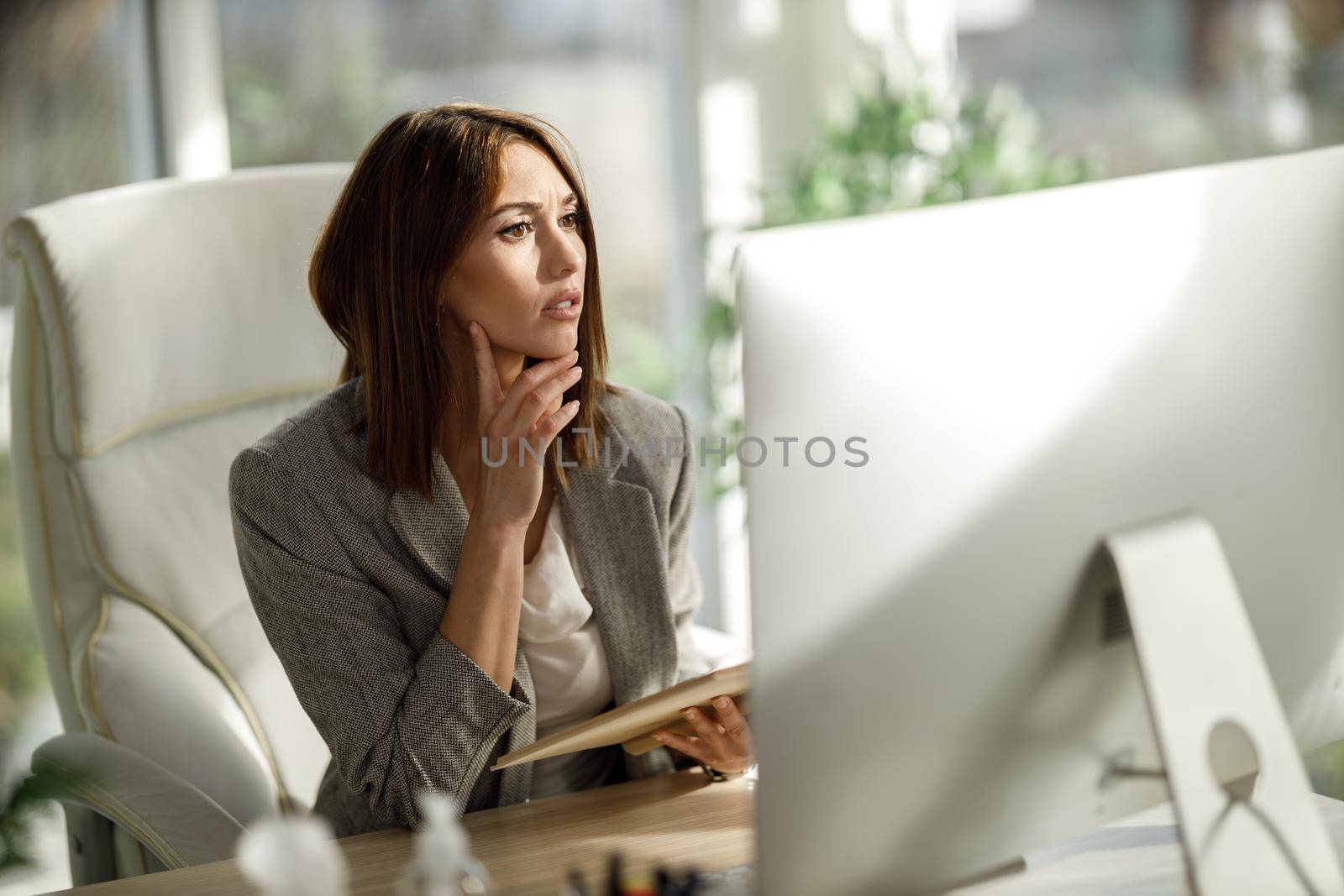 A pensive young woman sitting alone in her home office and working on computer.