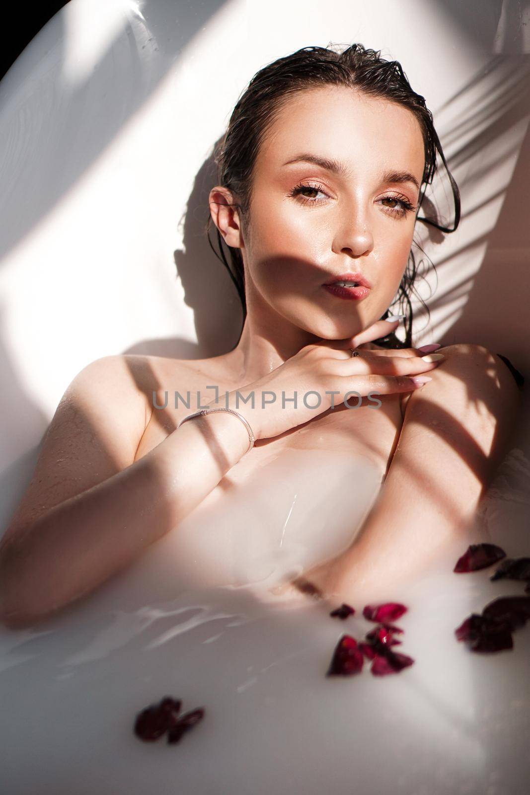 An Attractive girl relaxing in bath with petals on light background - fashion portrait