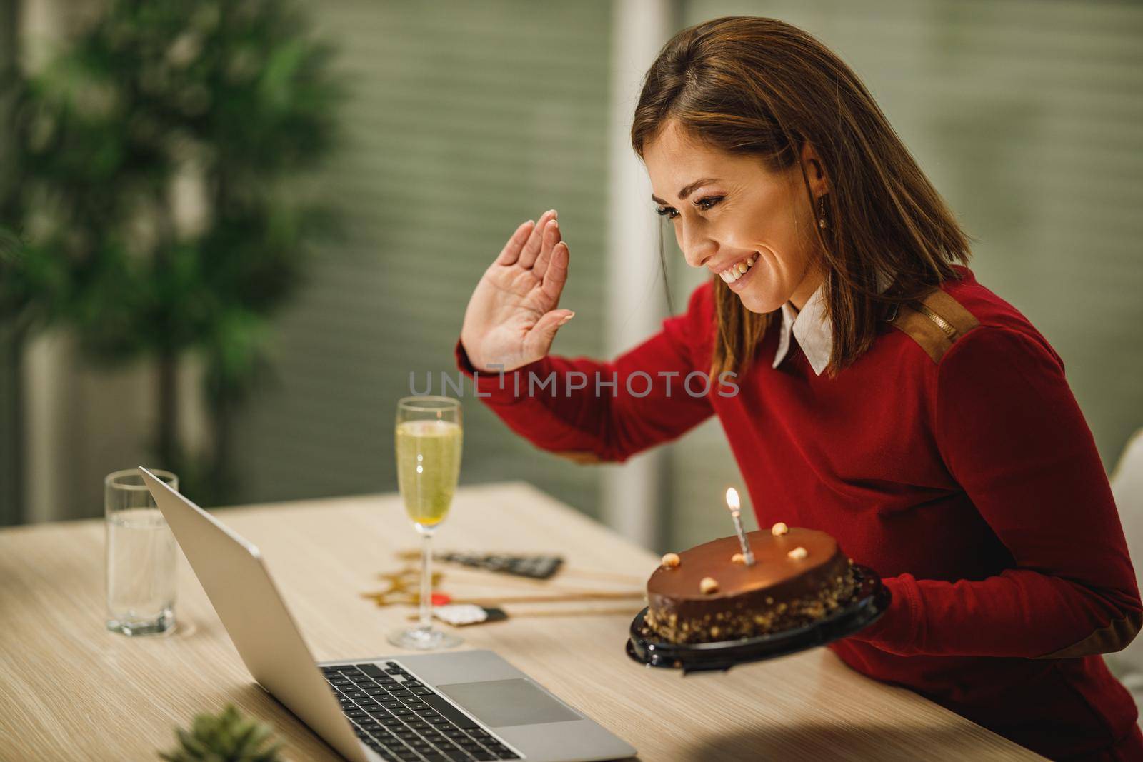 Smiling attractive woman holding birthday cake and have a online birthday party with friends.