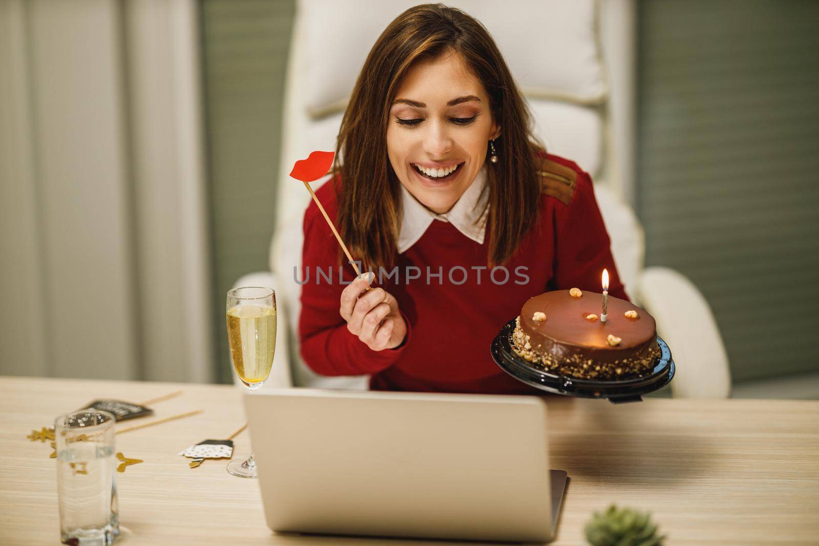 Smiling attractive woman holding a birthday cake and having a online party with friends during corona virus isolation.