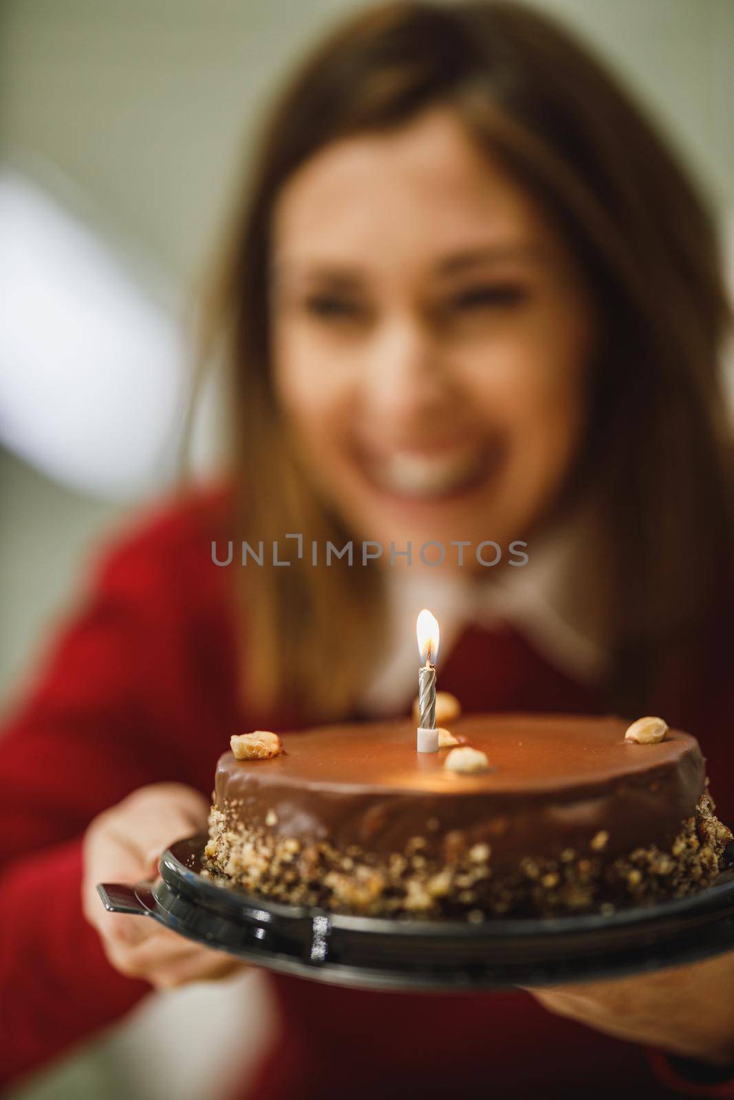 Cropped shot of a smiling woman holding a birthday cake with candles and having online party with friends.